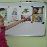 A girl points with a pointer at pictures on a magnetic board